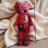 A pink Kawaii bear figurine with large ears and a stitched face is displayed on a cream-colored knitted blanket.