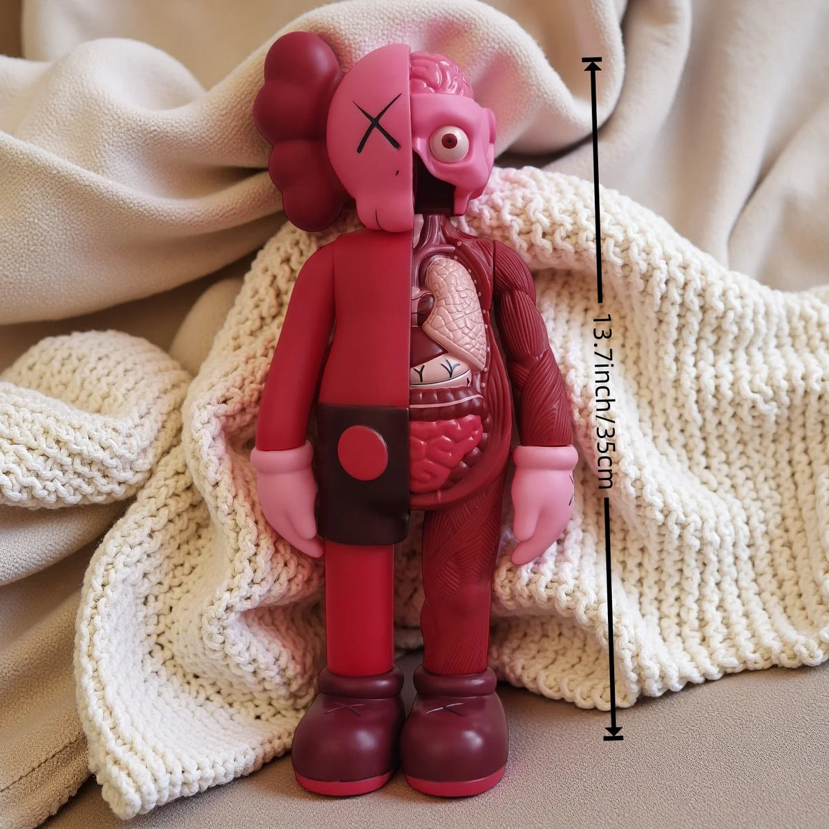 A pink Kawaii bear figurine with large ears and a stitched face is displayed on a cream-colored knitted blanket.
