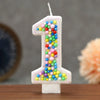 A white number one candle decorated with colorful candy beads for a birthday celebration.