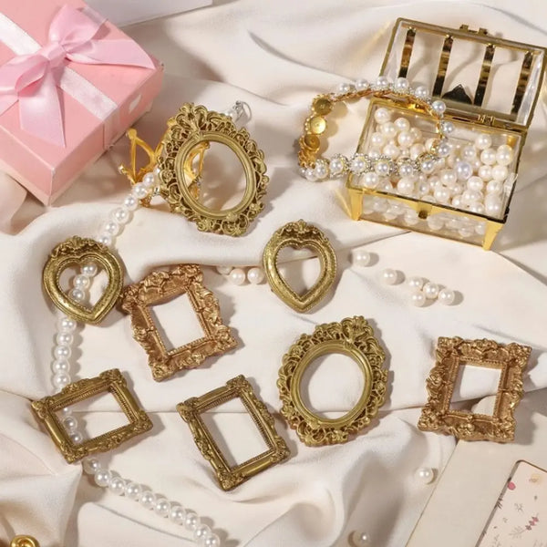 A collection of vintage gold and silver resin shadow box frames and pearl strands displayed on white fabric.