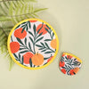 A round fabric hand fan with a yellow border featuring a pattern of orange and green leaves on a light background.