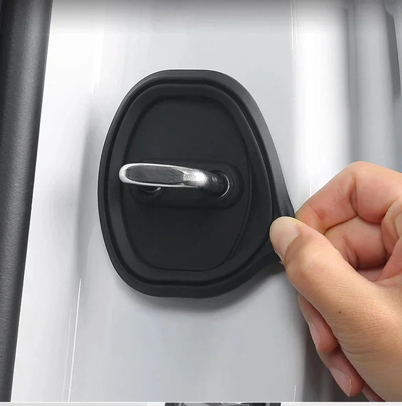 A hand is shown pressing a smooth, black silicone door lock protector on a white car door panel.