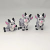 Three 3D printed goat figurines in gray and pink standing or lying down.