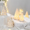 White ceramic glow-in-the-dark mini Christmas tree decor illuminated by warm lights on a snowy surface.