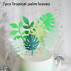 A cake decorated with green tropical palm leaves and foliage toppers.