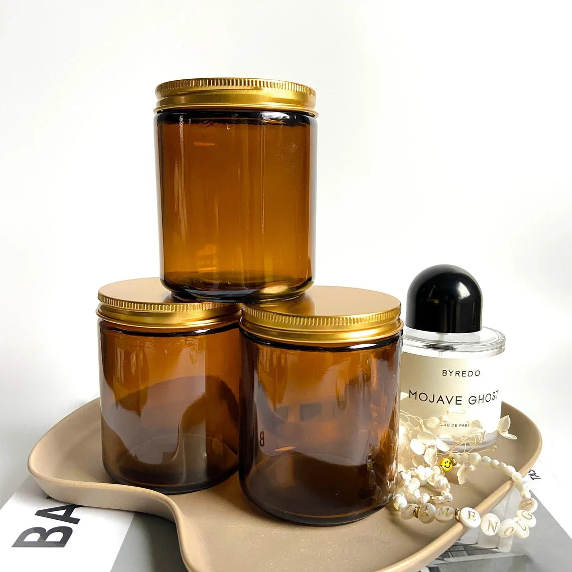 A set of two amber glass candle jars with gold metal lids resting on a light brown tray.