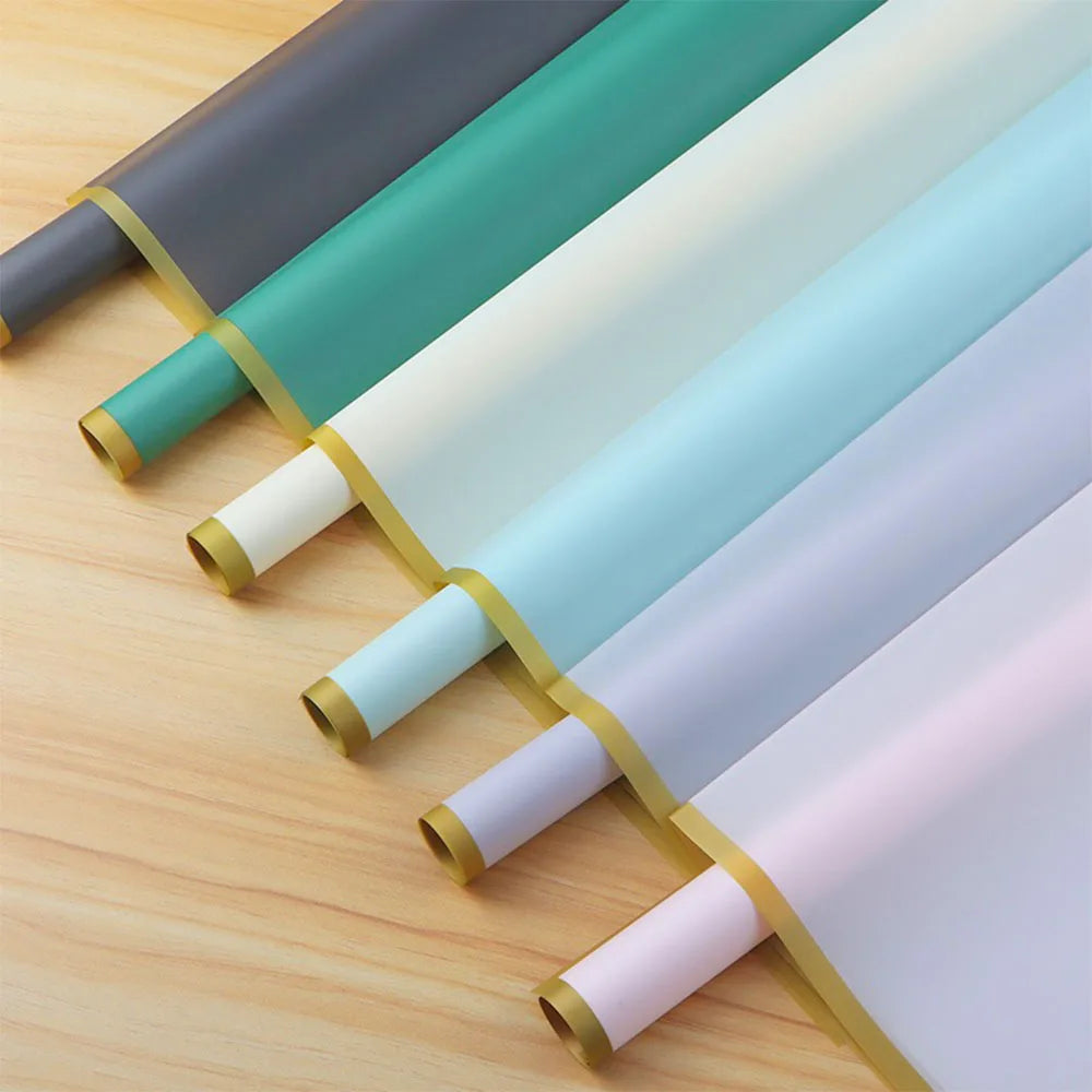 A set of ten rolls of gold edge floral wrapping paper in various shades of green, white, and light blue laid out on a wooden 