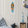 A wooden wall decor sign shaped like a surfboard featuring a tropical scene and the text Live in the Dream