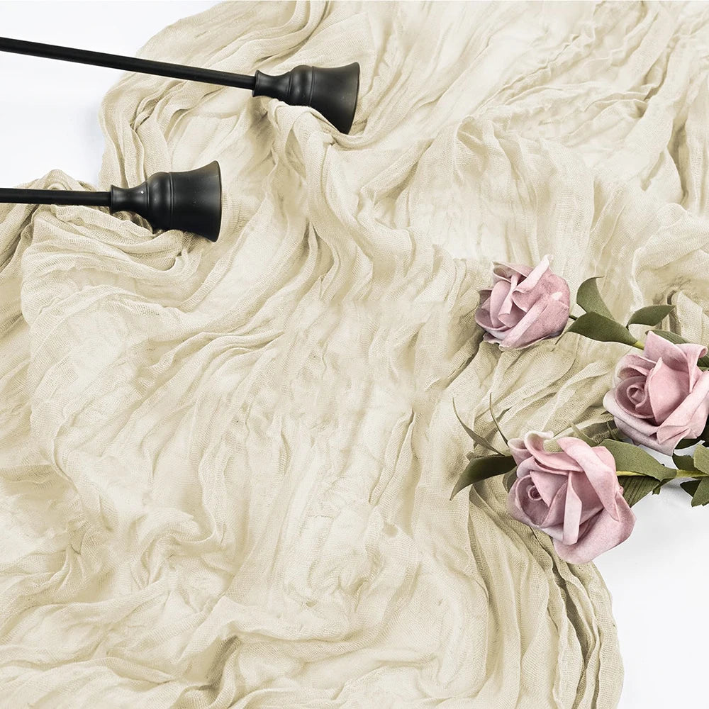 A light blue cheesecloth table runner is draped on a surface with dark, decorative metal utensils and pink roses.