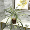 An artificial chlorophytum branch with long green leaves displayed on a white shelf.