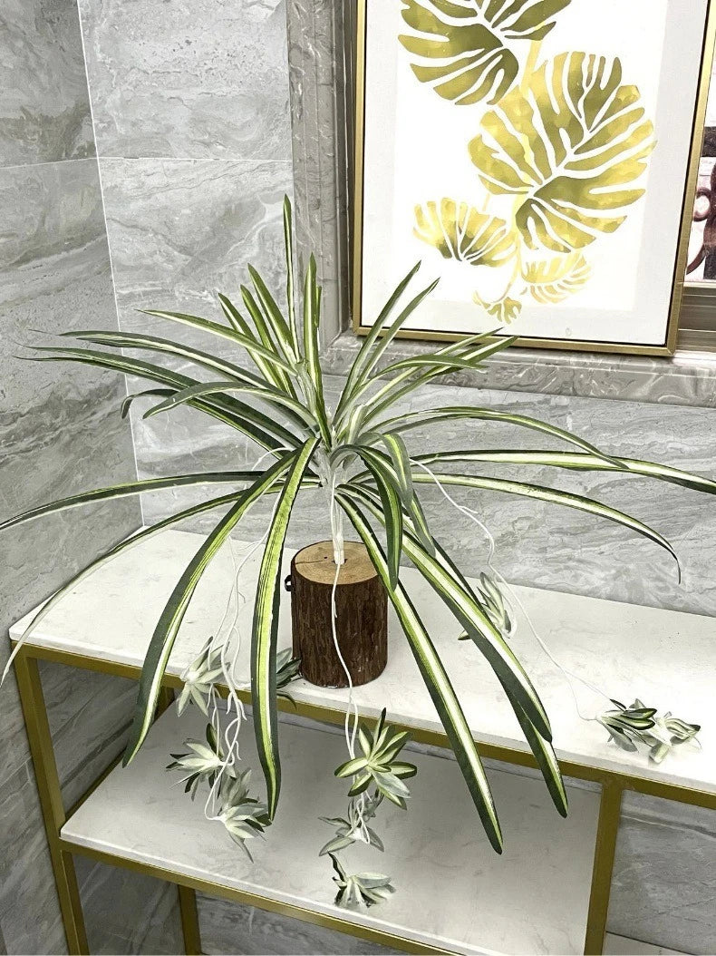 An artificial chlorophytum branch with long green leaves displayed on a white shelf.