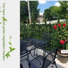 Black artificial ivy hedge fence panels growing vibrant red roses in a garden setting.