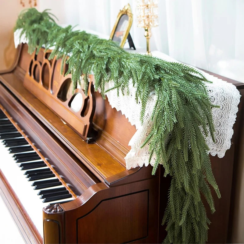 A realistic green Norfolk pine Christmas garland draped over a wooden piano.
