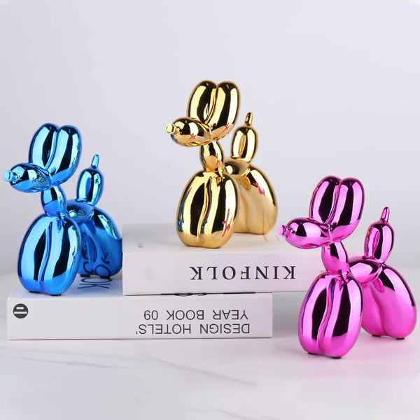 A set of resin balloon dog sculptures in gold and pink colors displayed on a white book.