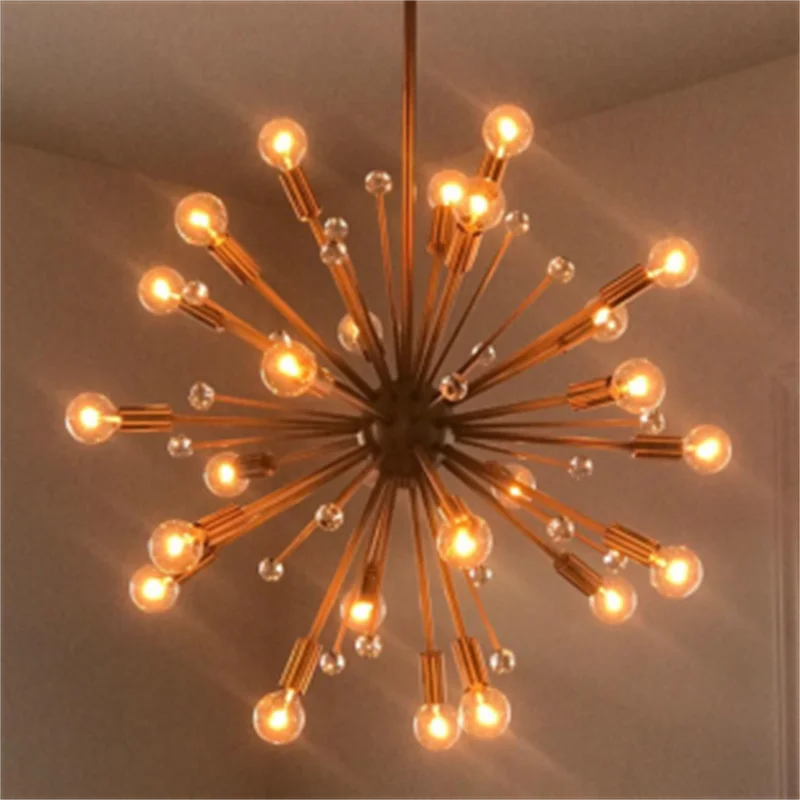 A modern chandelier with multiple arms and exposed filament bulbs hangs against a light wall.