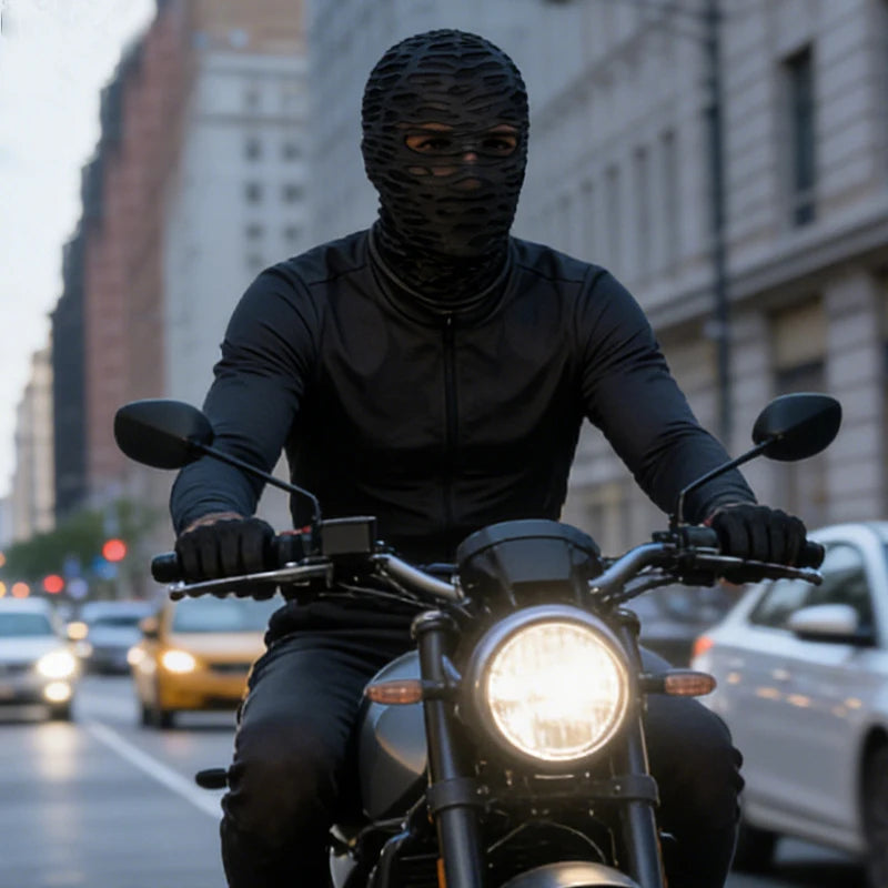 A person wearing a black mesh balaclava face mask riding a motorcycle on a city street.