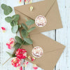 A kraft paper envelope is decorated with gold foil thank you seals and green eucalyptus leaves.