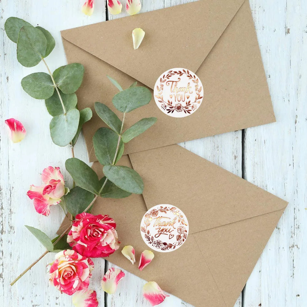 A kraft paper envelope is decorated with gold foil thank you seals and green eucalyptus leaves.