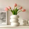 A vase of pink tulips in a white ceramic pot on a light shelf.
