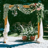 An archway decorated with greenery and flowers, featuring a white drape, set outdoors.