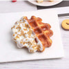 A golden waffle topped with white cream and chopped nuts served on a white plate.