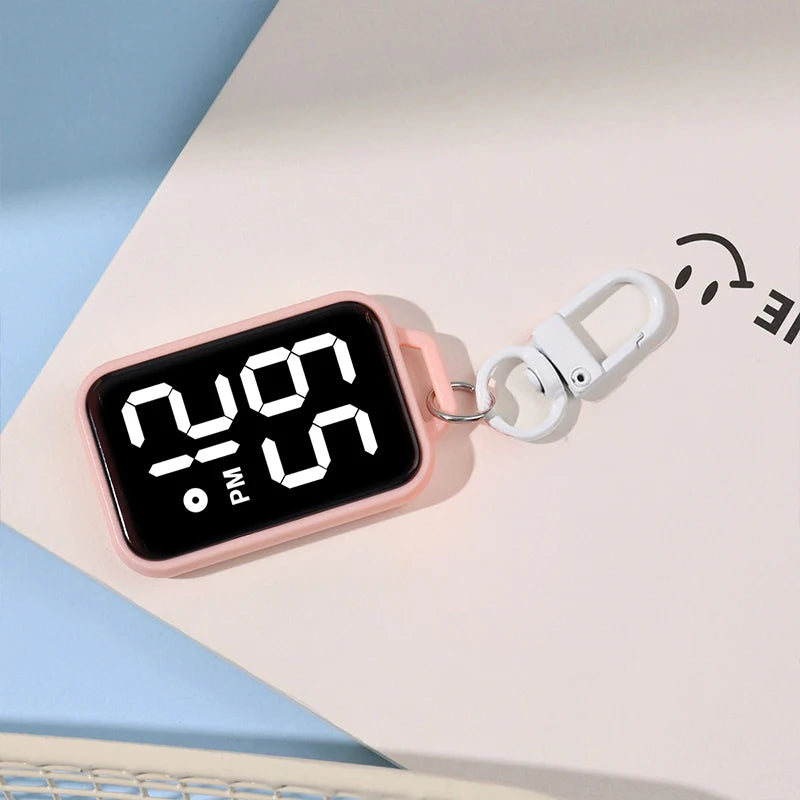 A pink LED keychain pocket watch with a digital display showing 12:00 PM on a white surface.