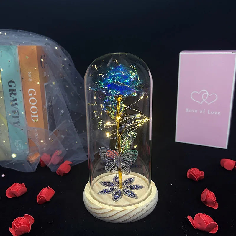 A clear glass dome containing a crystal rose flower is displayed on a stand, surrounded by red rose petals.