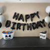 A banner of black and white foil letter balloons spelling out HAPPY BIRTHDAY decorated on a beige wall.