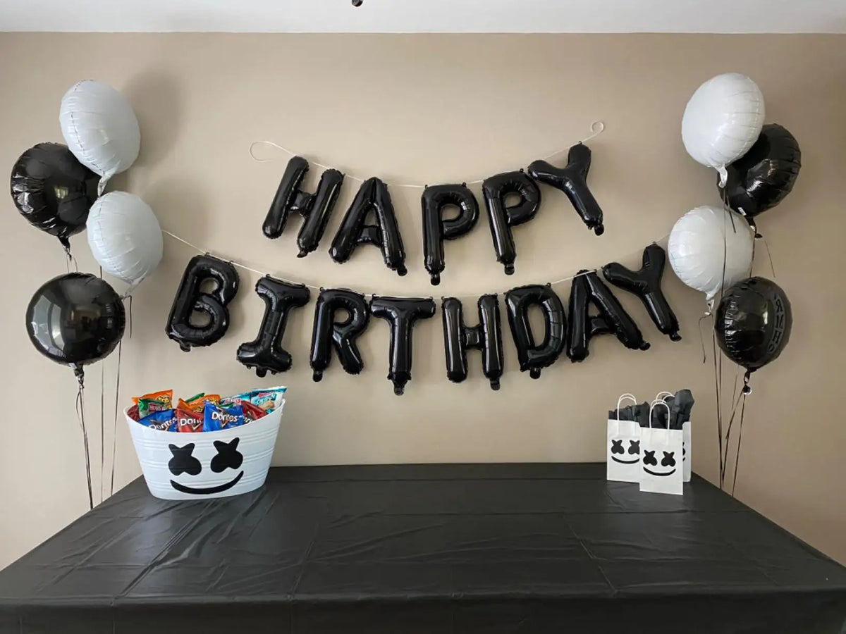 A banner of black and white foil letter balloons spelling out HAPPY BIRTHDAY decorated on a beige wall.