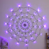 A glowing purple spider web pattern made of LED string lights on a white wall.
