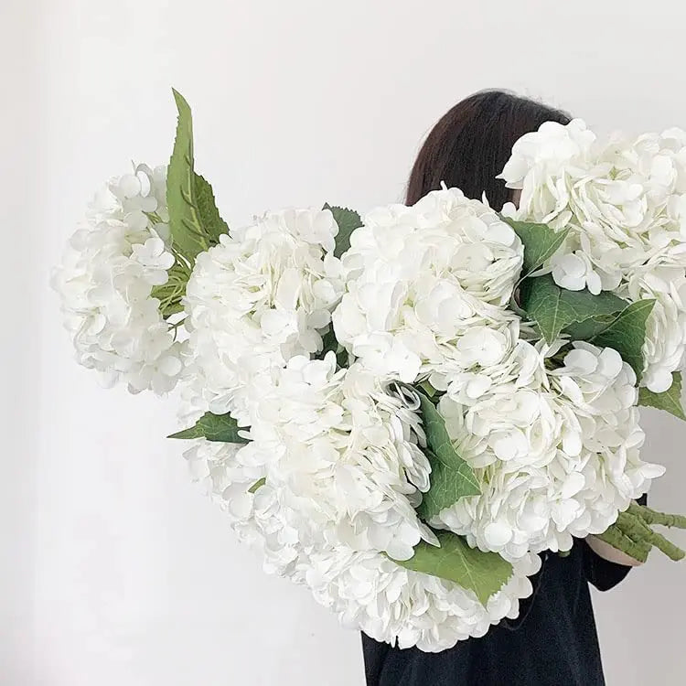 A large bouquet of white artificial hydrangea flowers with green leaves.