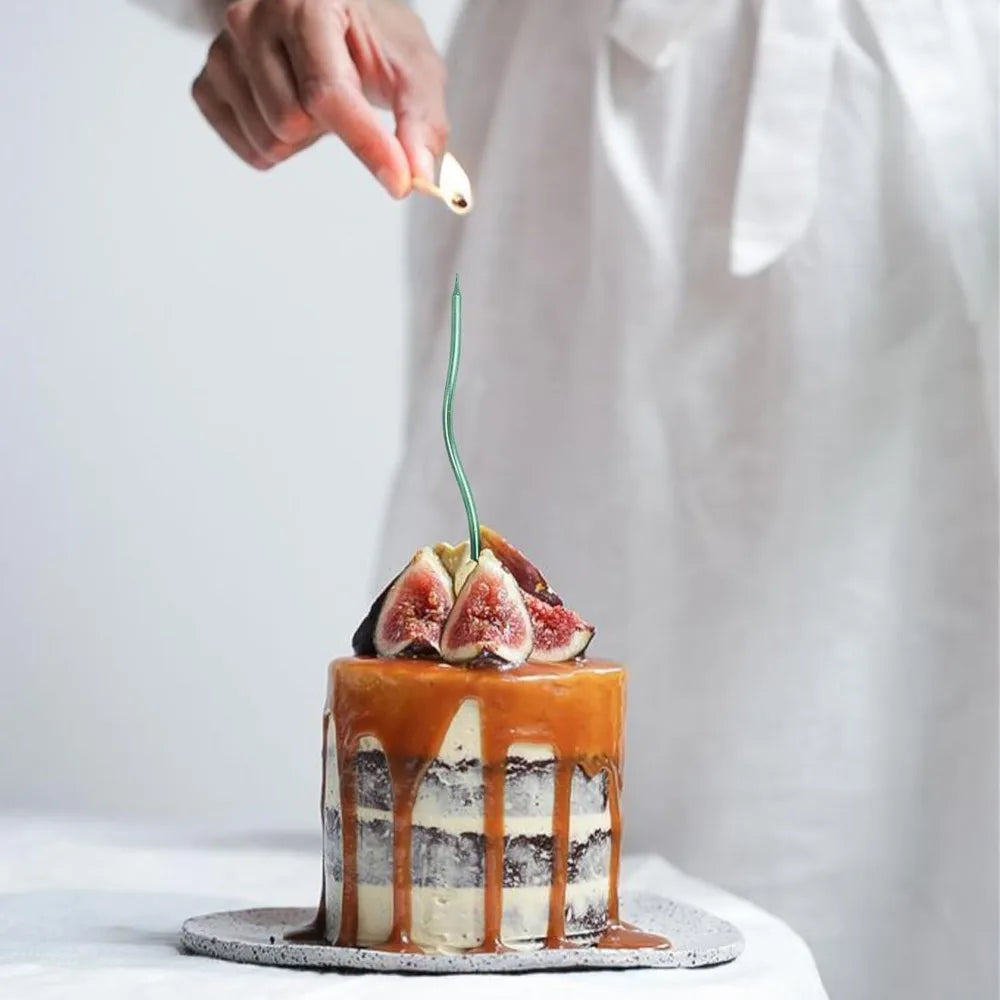 A hand is placing a thin green candle on top of an elegant spiral cake decorated with figs and caramel drizzle.