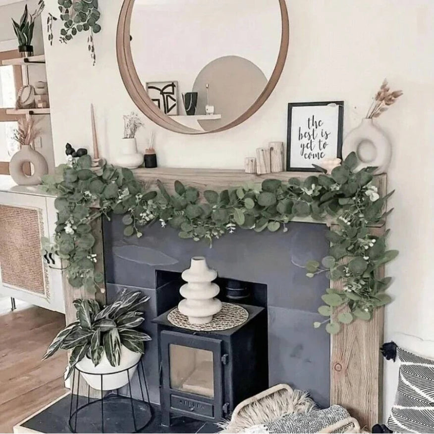 An artificial eucalyptus garland with white flowers draped across a fireplace mantel and surrounding decor.