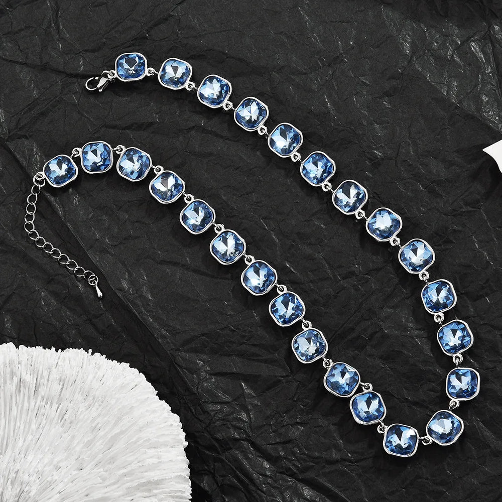 A delicate blue crystal pendant necklace with a silver chain and lobster claw clasp displayed on black fabric.