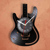 A black electric guitar body is used as a wall clock, featuring a vinyl record face with hands and a red indicator.