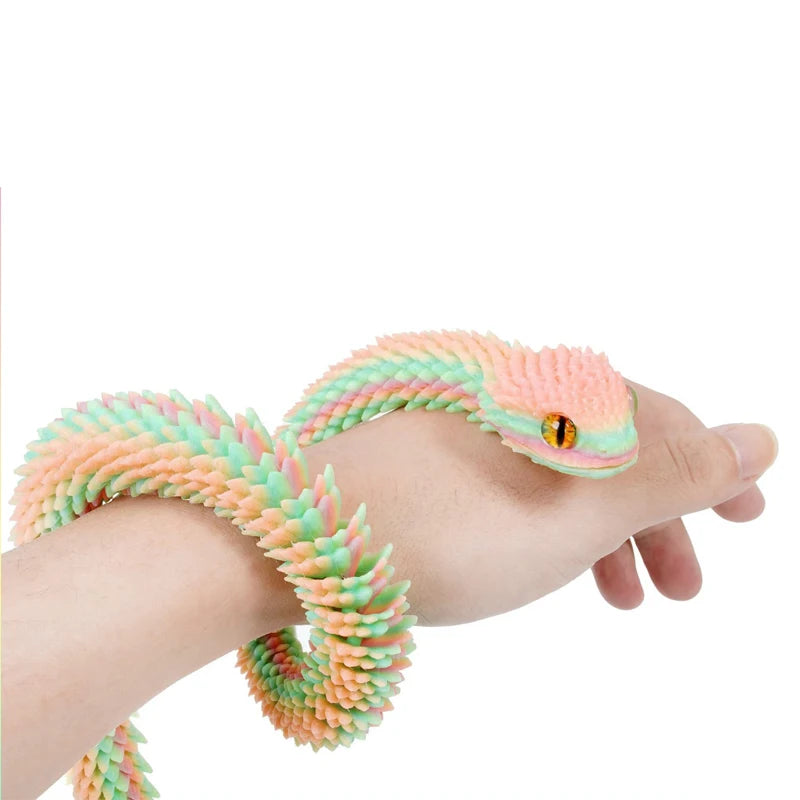 Eine Hand hält ein flexibles, buntes 3D gedrucktes Schlangen-Fidget-Spielzeug mit rosa und grünen Schuppen.