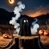 A black ghost figurine with wisps of smoke sits on a wooden log in a dark outdoor setting under a moonlit sky.