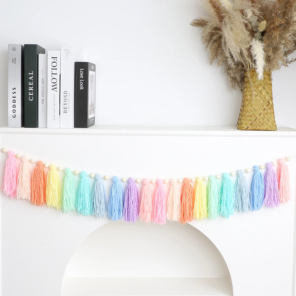 Handmade boho rainbow tassel garland with wooden beads displayed on a white mantelpiece.