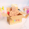 A humorous 3D pop-up birthday card featuring a male figure, heart balloons, and confetti inside a cardboard box.