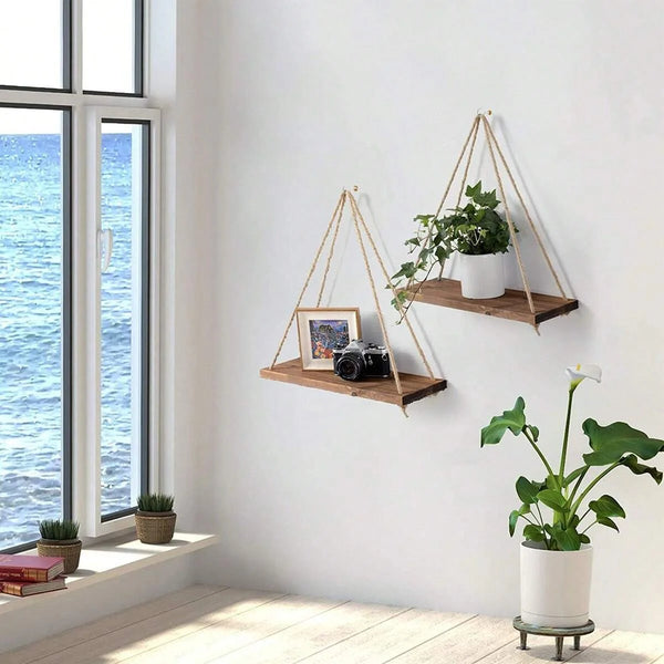 A wooden hanging shelf with hemp rope is mounted on a white wall, displaying potted plants and decor.