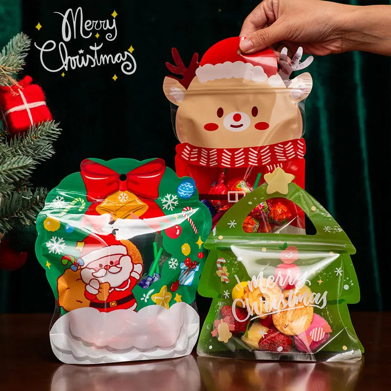 A hand is placing a reusable green Christmas gift bag filled with treats and party favors onto a wooden surface.