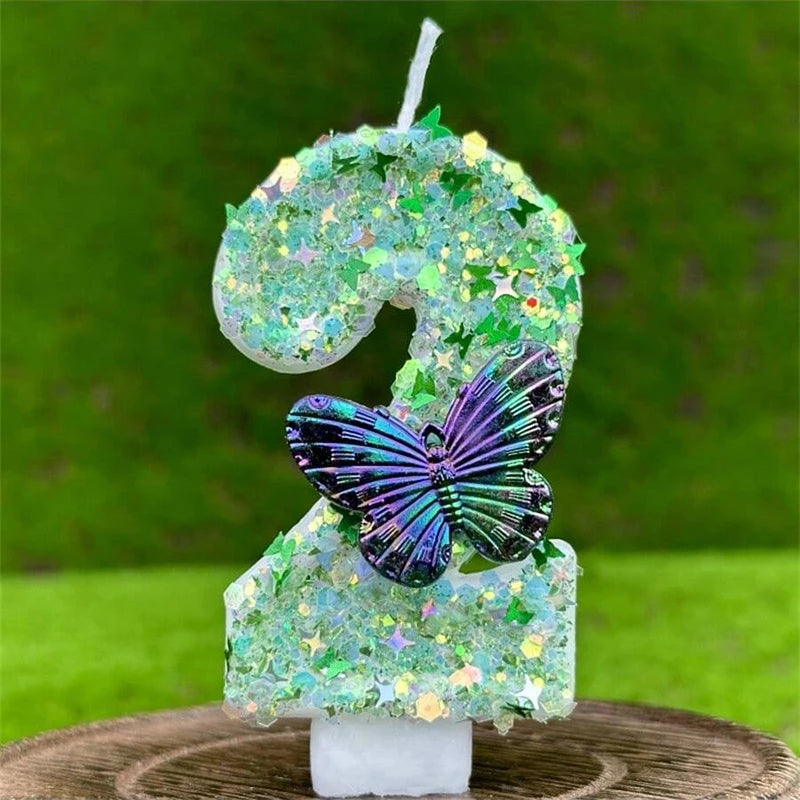 A number candle shaped like a 2, covered in green sequins and featuring a purple butterfly decoration.