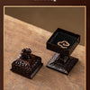 A dark brown ceramic incense burner featuring a detailed square design, shown on a wooden surface.