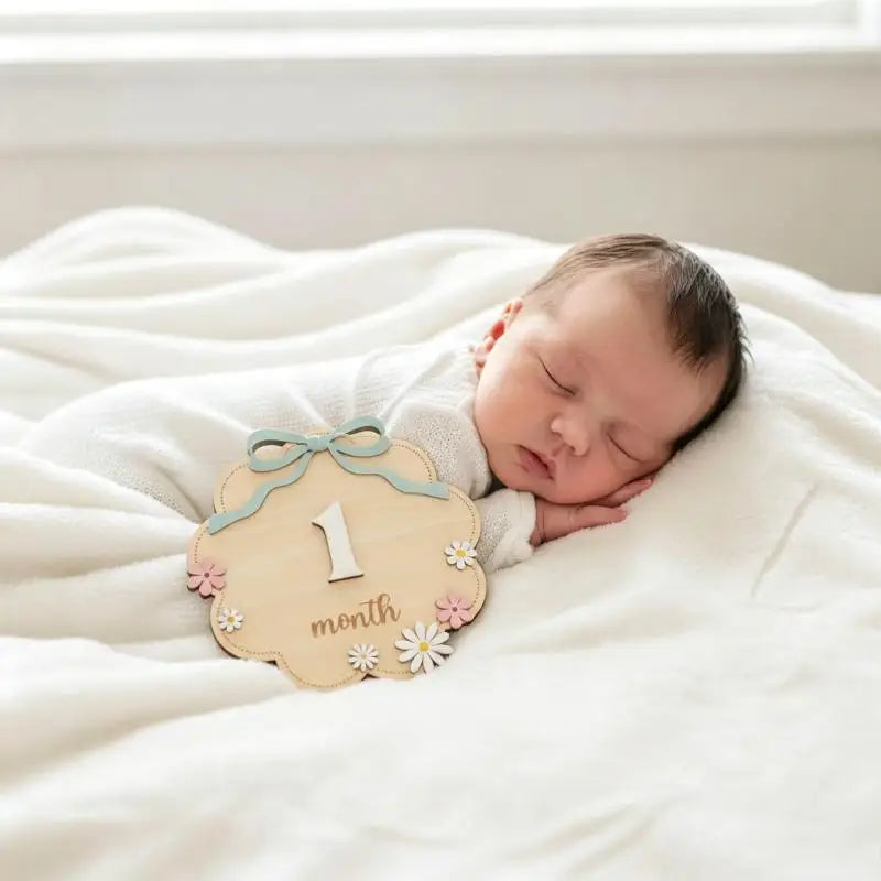 Neugeborenes Baby schläft auf einer weißen Decke neben einem natürlichen Holz-Meilenstein mit der Zahl eins