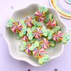 A white dish holds numerous colorful, striped candy resin cabochons in pink, green, and yellow hues.