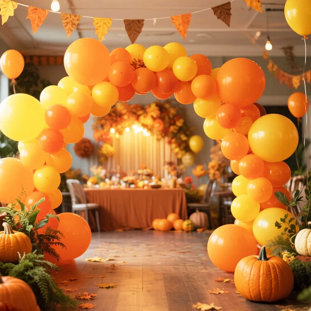 A vibrant archway made of orange and yellow latex balloons decorated with autumn foliage and pumpkins.