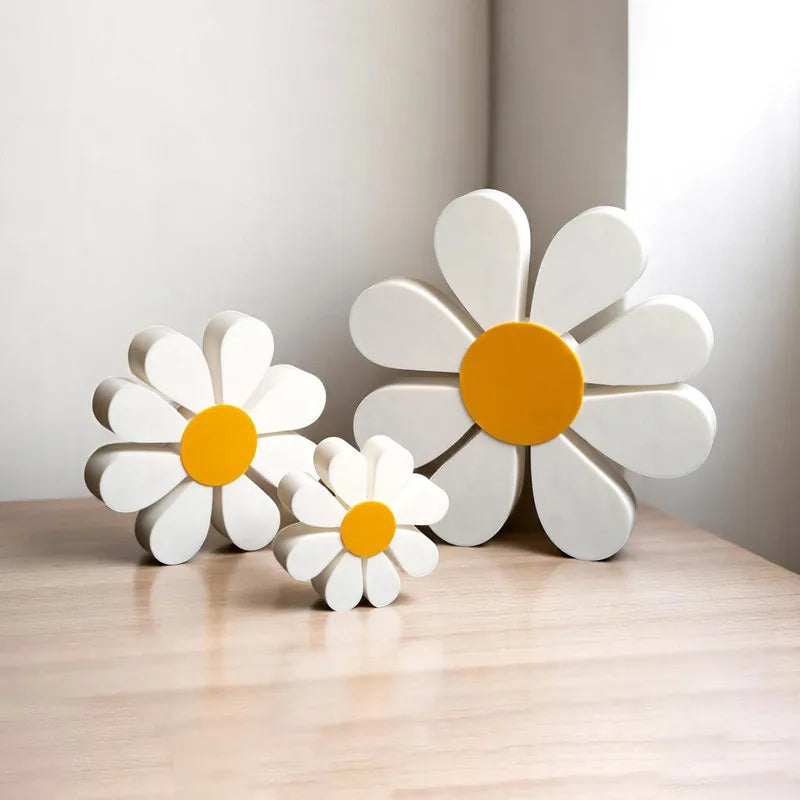 Set of three white and orange wooden daisy flower ornaments displayed on a light wood surface.