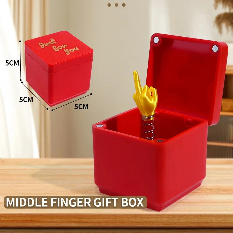 Boîte cadeau rouge avec un doigt d'honneur doré, posée sur une surface en bois.