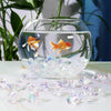 A glass bowl filled with crushed diamond acrylic pebbles containing a small orange fish.