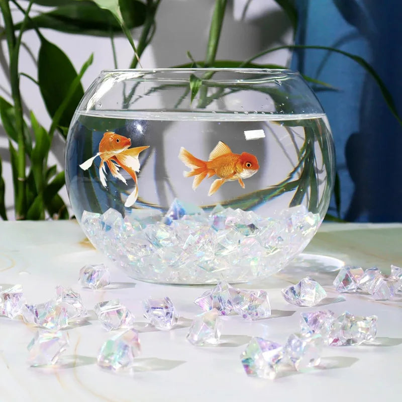 A glass bowl filled with crushed diamond acrylic pebbles containing a small orange fish.